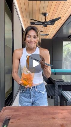 a woman standing in front of a wooden table holding a jar of oranges and looking at the camera