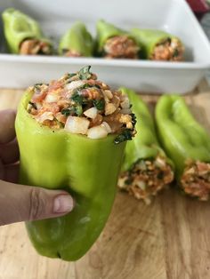 a person holding up a green pepper with other peppers in the background