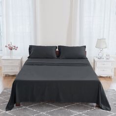 a bed with black sheets and pillows in a room next to two white nightstands