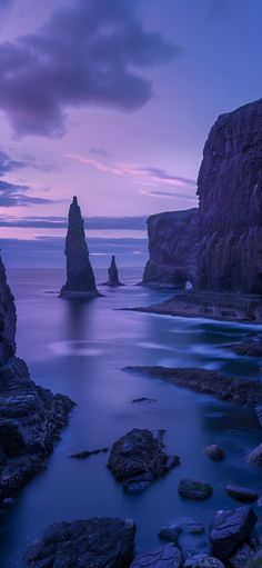 the ocean is full of rocks and water at dusk with purple clouds in the sky