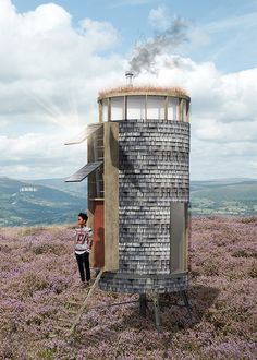 a man standing in front of a tower on top of a hill next to purple flowers