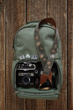 a camera and some other items in a green bag on a wooden surface with a brown strap