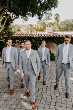 a group of men in suits and ties walking down a brick walkway with trees behind them