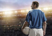 a man holding a soccer ball in front of a stadium filled with people at night