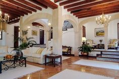 a living room filled with furniture and chandeliers on top of wooden ceiling beams