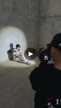 a man taking a photo of a person sitting on a bench in front of a wall