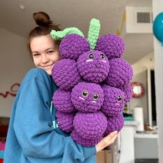 a woman holding a bunch of purple crocheted fruit