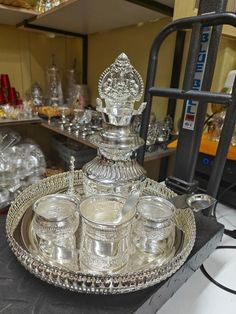 an ornate silver tray with four glasses on it in front of other glassware and bottles