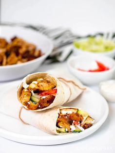 two wraps filled with meat and vegetables sitting on a plate next to bowls of salad