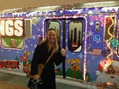 a woman is standing in front of a train decorated with christmas lights and holiday decorations