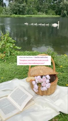 an open book sitting on top of a blanket next to a basket filled with flowers