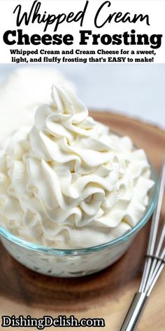 whipped cream is in a glass bowl on a wooden plate with two spoons next to it