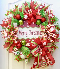 a christmas wreath with red and green decorations on the front door, hanging from a white door