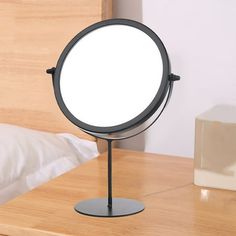 a round mirror on a stand in front of a white pillow and wooden headboard