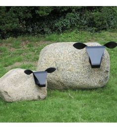 two black sheep sculptures sitting on top of a green grass covered field next to a large rock