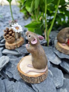 a mouse figurine sitting on top of a tree stump next to some flowers