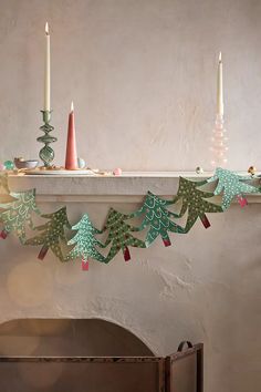 a mantle with candles and paper christmas trees on it in front of a fireplace mantel