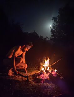 a man kneeling over a campfire at night