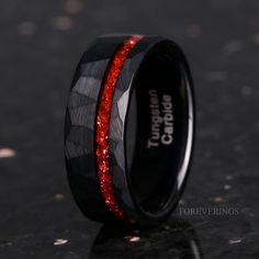 black ceramic ring with red glitter inlays on the outside and inside, sitting on a dark surface