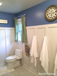 a white toilet sitting next to a bathroom sink under a clock mounted on the wall