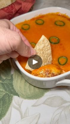 a person dipping tortilla chips into a bowl of soup