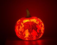 a carved pumpkin with leaves on it sitting on a table in front of a red background