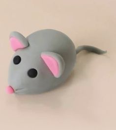 a gray and pink toy mouse on a white surface with one eye open, the other half closed