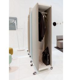 an open closet with clothes and handbags on wheels in a white room, next to a couch