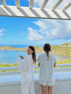 two girls standing on a balcony looking out at the ocean