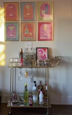 a bar cart with drinks on it in front of four framed art pieces hanging on the wall