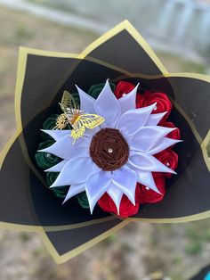 a paper flower with a butterfly sitting on it's center and the petals are red, white, and green