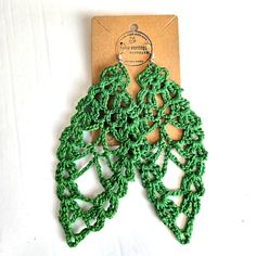 a pair of green crocheted earrings on top of a piece of cardboard paper