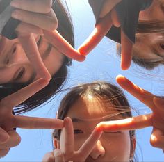 four girls making peace signs with their hands in the shape of fingers, against a blue sky background