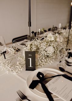 the table is set with black and white place settings, silverware, and baby's breath flowers