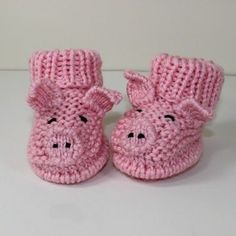 pink knitted baby booties with black eyes and nose on white table top next to wall