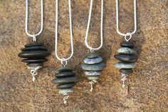 four necklaces with different types of stones hanging from it's hooks on a stone surface