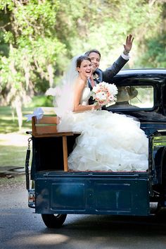 a bride and groom are riding in the back of an old truck with their hands up