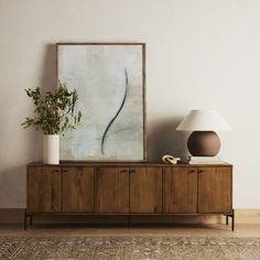 a painting on the wall next to a wooden cabinet with a lamp and plant in it