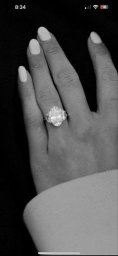 a woman's hand with a diamond ring on her left hand and white nails