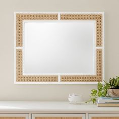 a mirror on the wall above a dresser with drawers and a plant next to it