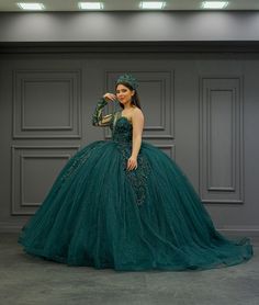 a woman in a green ball gown standing next to a gray wall and wearing a tiara