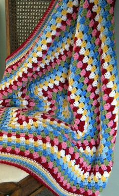 a crocheted blanket sitting on top of a chair next to a wooden chair