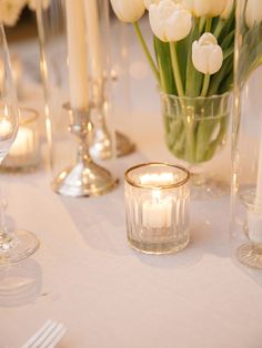 white tulips and candles sit in glass vases on a table