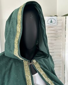 This classic design suits lots of cosplay characters and the fabric is crease resistant and drapes beautifully. This stunning cape is offered in emerald green or forest green.  It features a pointy hood, beautiful embellishment along the edges & a matching clasp at the neck. The back length of the cape measures approximately 70cms from the nape of the neck.  I am a very experienced cosplay cape and cloak designer with lots of designs and experience to help me create the garment that often puts t Cloak Designs Hooded Capes, Gothic Hooded Cape For Costume, Hooded Gothic Cape For Costume, Gothic Cape For Cosplay Events, Elven Style Cape For Costume Party, Cape Costumes For Cosplay And Fantasy Events, Elven Cape For Costume Party, Cosplay Cape Costume For Fantasy Events, Fantasy Cape Costume For Cosplay Events