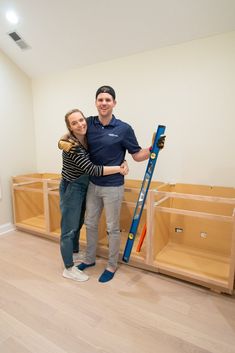 a man and woman standing next to each other in a room with wooden shelves holding skis