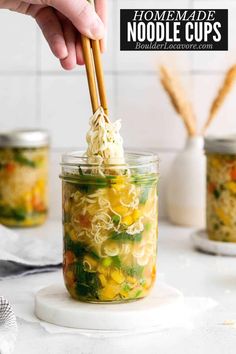 someone holding chopsticks over a jar filled with noodle soup and noodles in it