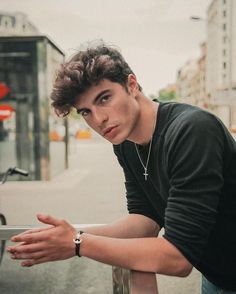 a young man leaning on a rail in the city with his hand resting on it