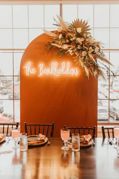 the table is set with place settings and flowers on it, along with an orange backdrop