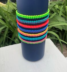 a stack of multicolored bracelets sitting on top of a blue cup next to plants