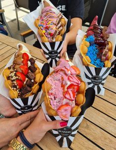 four different types of desserts in paper baskets on a table with people sitting around